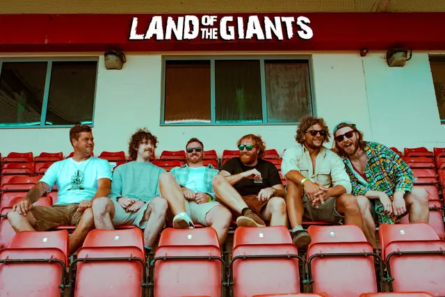 Land of the Giants sat on seats in a football stand.